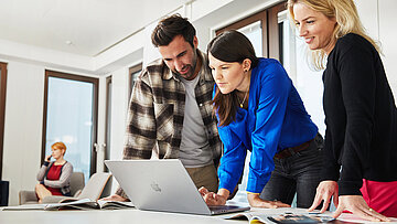 Drei Menschen schauen auf ein Laptop